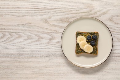 Photo of Toast with tasty pistachio butter, banana slices, blueberries and nuts on white wooden table, top view. Space for text