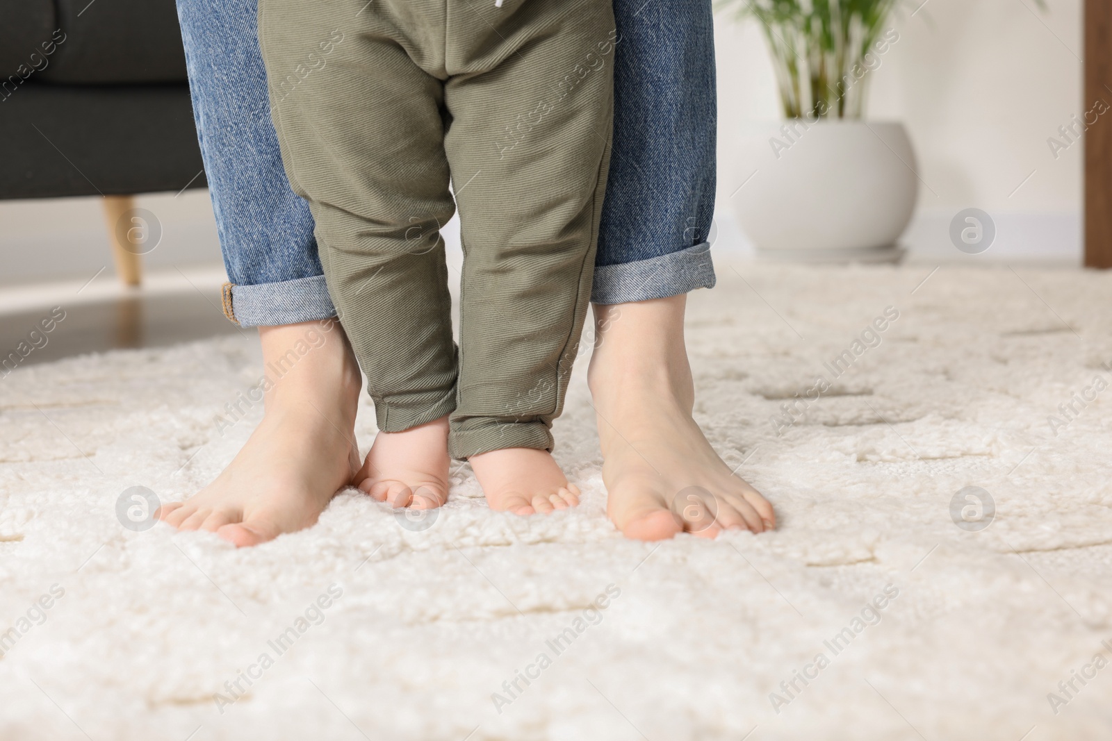 Photo of Mother supporting her baby son while he learning to walk on carpet at home, closeup