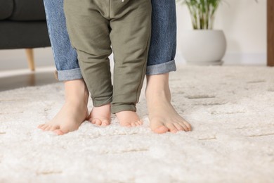 Mother supporting her baby son while he learning to walk on carpet at home, closeup