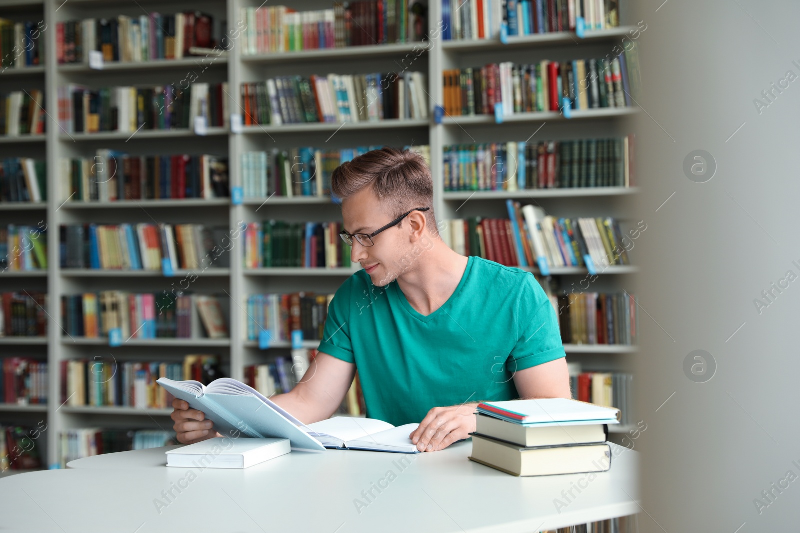 Photo of Young man reading book at table in library