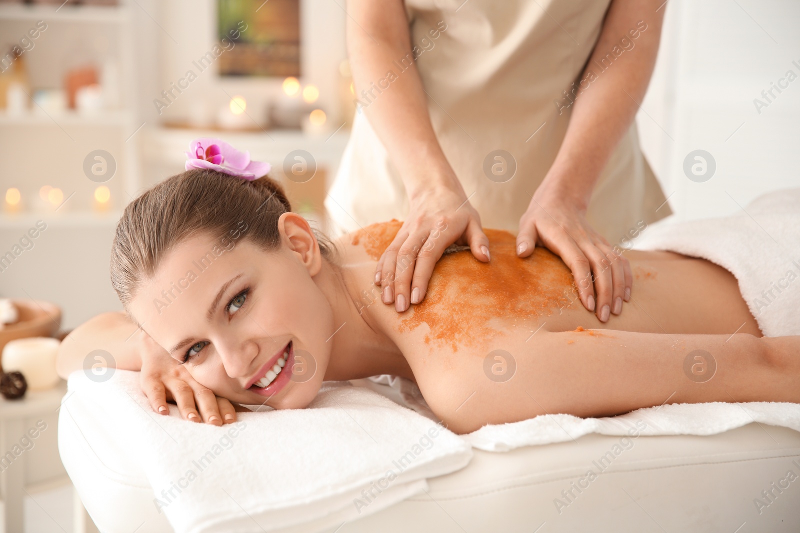 Photo of Beautiful young woman having massage with body scrub in spa salon