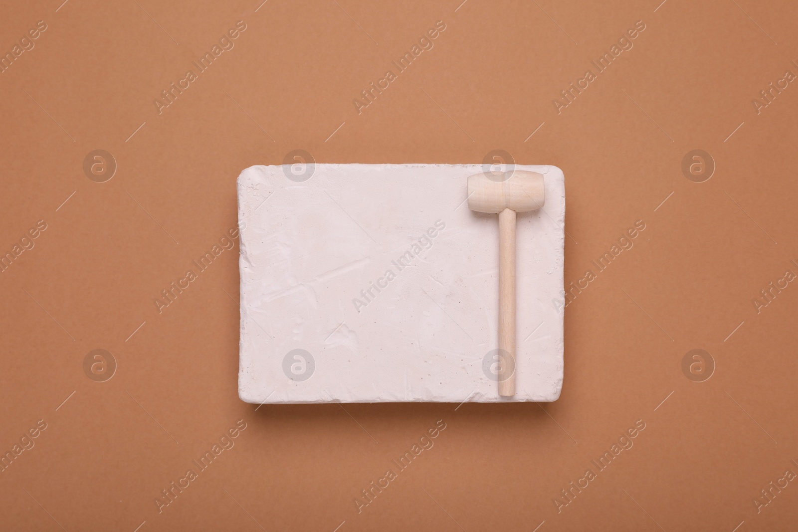 Photo of Educational toy for motor skills development. Excavation kit (plaster and wooden mallet) on brown background, top view