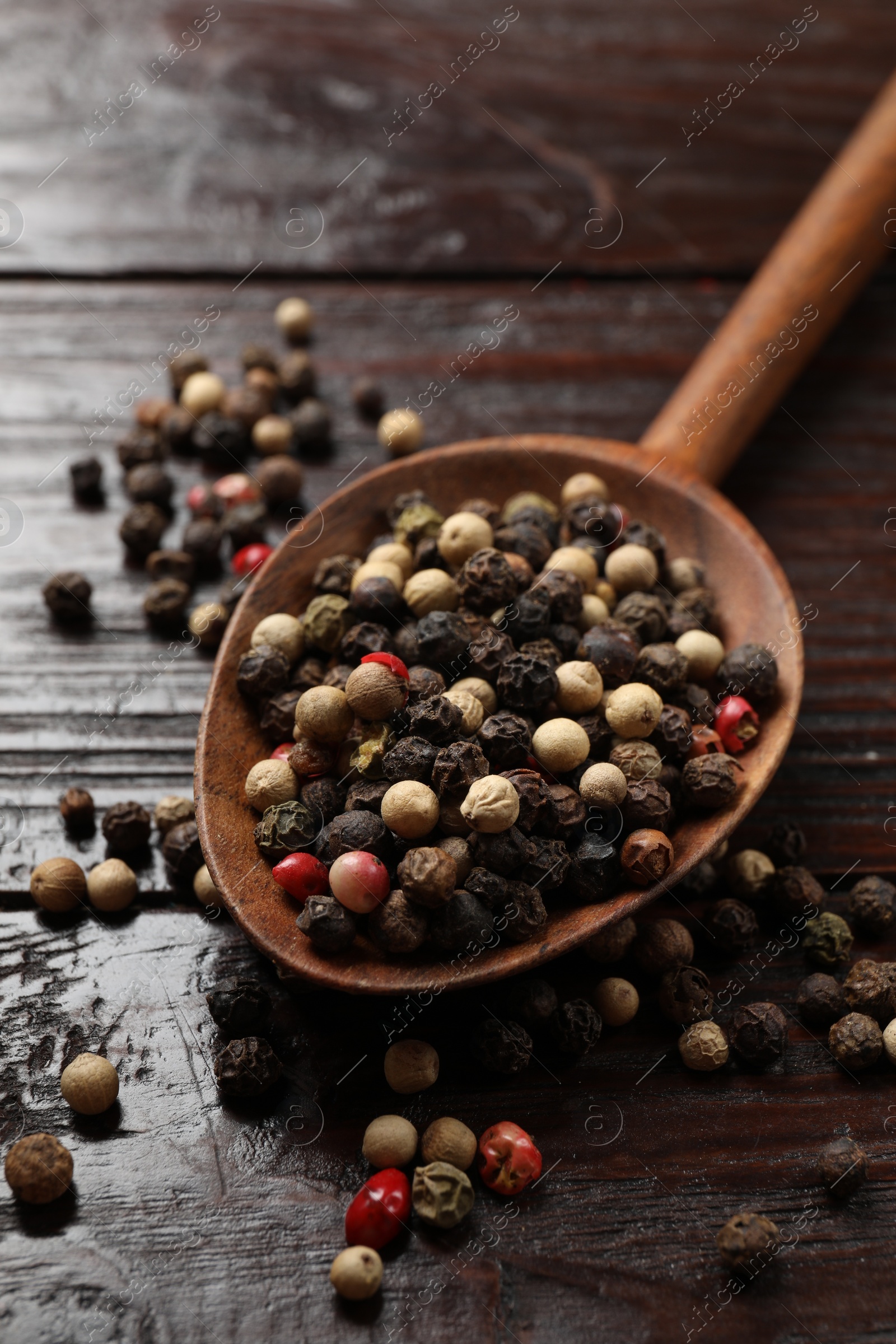 Photo of Aromatic spice. Different peppers in spoon on black table, closeup