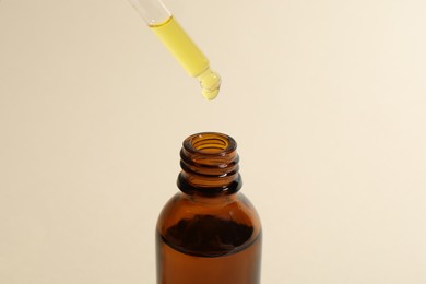 Dripping cosmetic oil from pipette into bottle on beige background, closeup