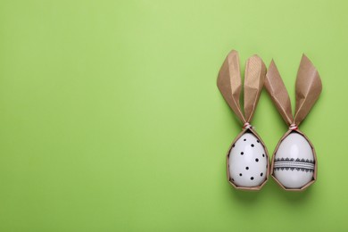 Photo of Easter bunnies made of craft paper and eggs on light green background, flat lay. Space for text