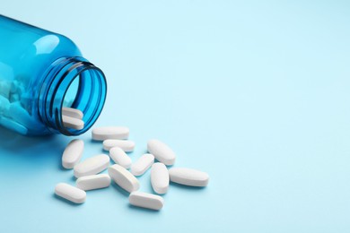 Vitamin pills and bottle on light blue background, closeup. Space for text