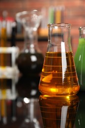 Photo of Laboratory glassware with different types of oil on mirror table, closeup