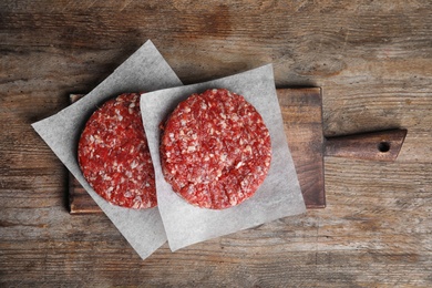 Raw meat cutlets for burger on wooden table, top view