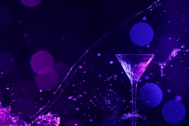 Photo of Pouring martini. Glass and splashes in neon lights on dark blue background, bokeh effect with space for text