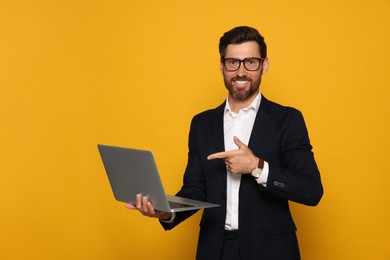 Photo of Smiling bearded man pointing at laptop on orange background