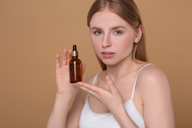 Beautiful young woman with bottle of essential oil on brown background