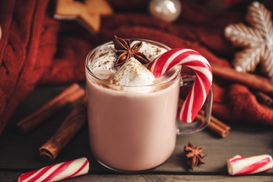 Glass cup of tasty cocoa with marshmallows and Christmas candy cane on wooden table