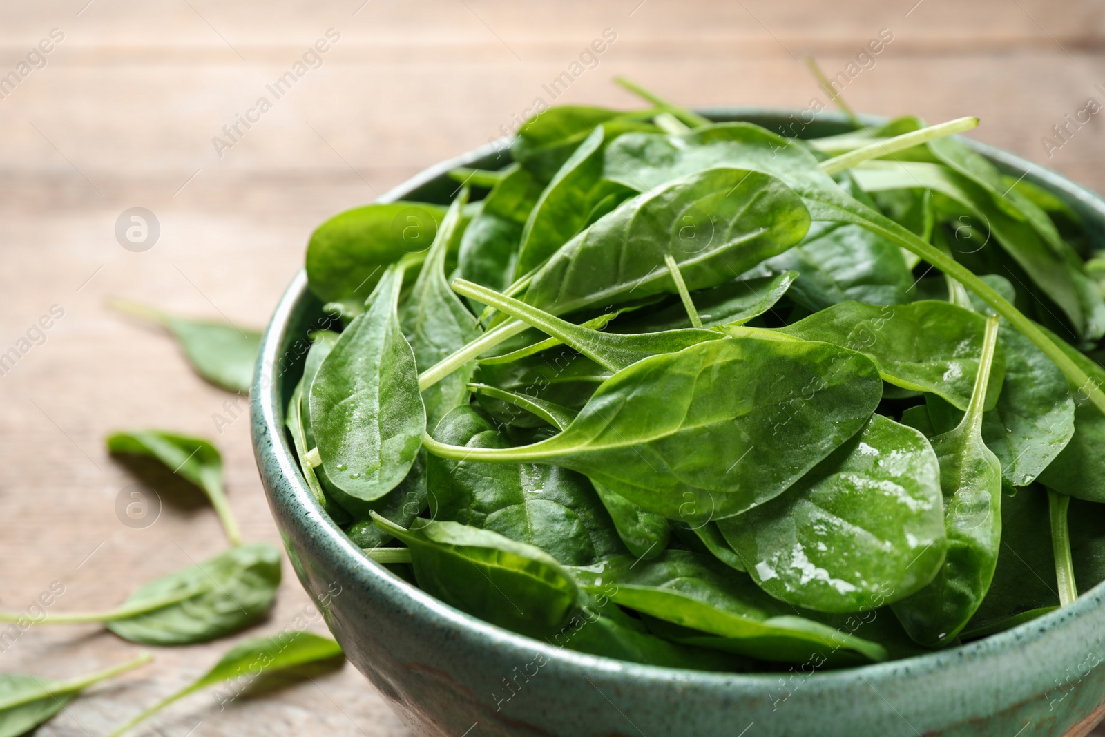 Photo of Bowl of fresh green healthy spinach on wooden table, closeup