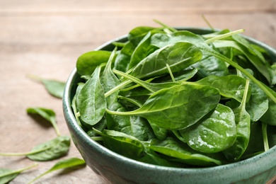 Photo of Bowl of fresh green healthy spinach on wooden table, closeup