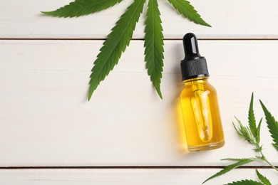 Photo of Bottle of CBD oil and fresh hemp leaves on white wooden table, flat lay. Space for text