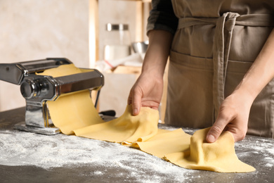Photo of Woman preparing dough with pasta maker machine at grey table, closeup