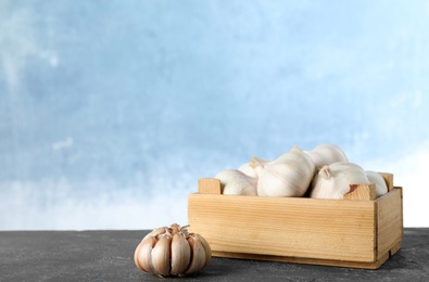 Photo of Wooden crate full of fresh garlic on table against color background, space for text