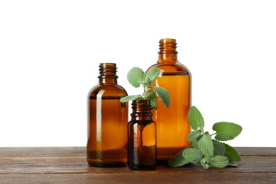 Photo of Bottles of essential oil and mint on wooden table against white background