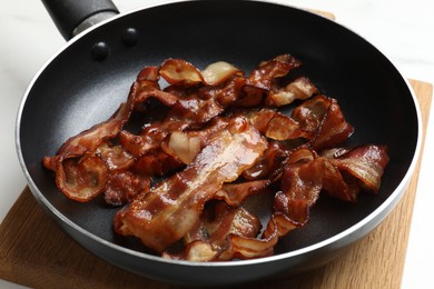 Photo of Delicious bacon slices in frying pan on white table, closeup