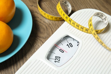 Photo of Scales, measuring tape and oranges on wooden background, closeup. Weight loss