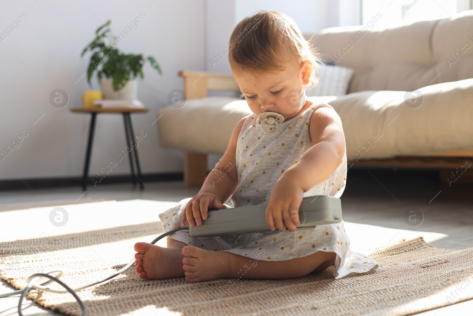 Photo of Baby girl playing with power strip on floor at home. Dangerous situation