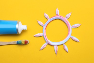 Photo of Sun made with toothpaste, brush and tube on yellow background, flat lay