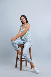 Photo of Beautiful young woman sitting on stool against light grey background