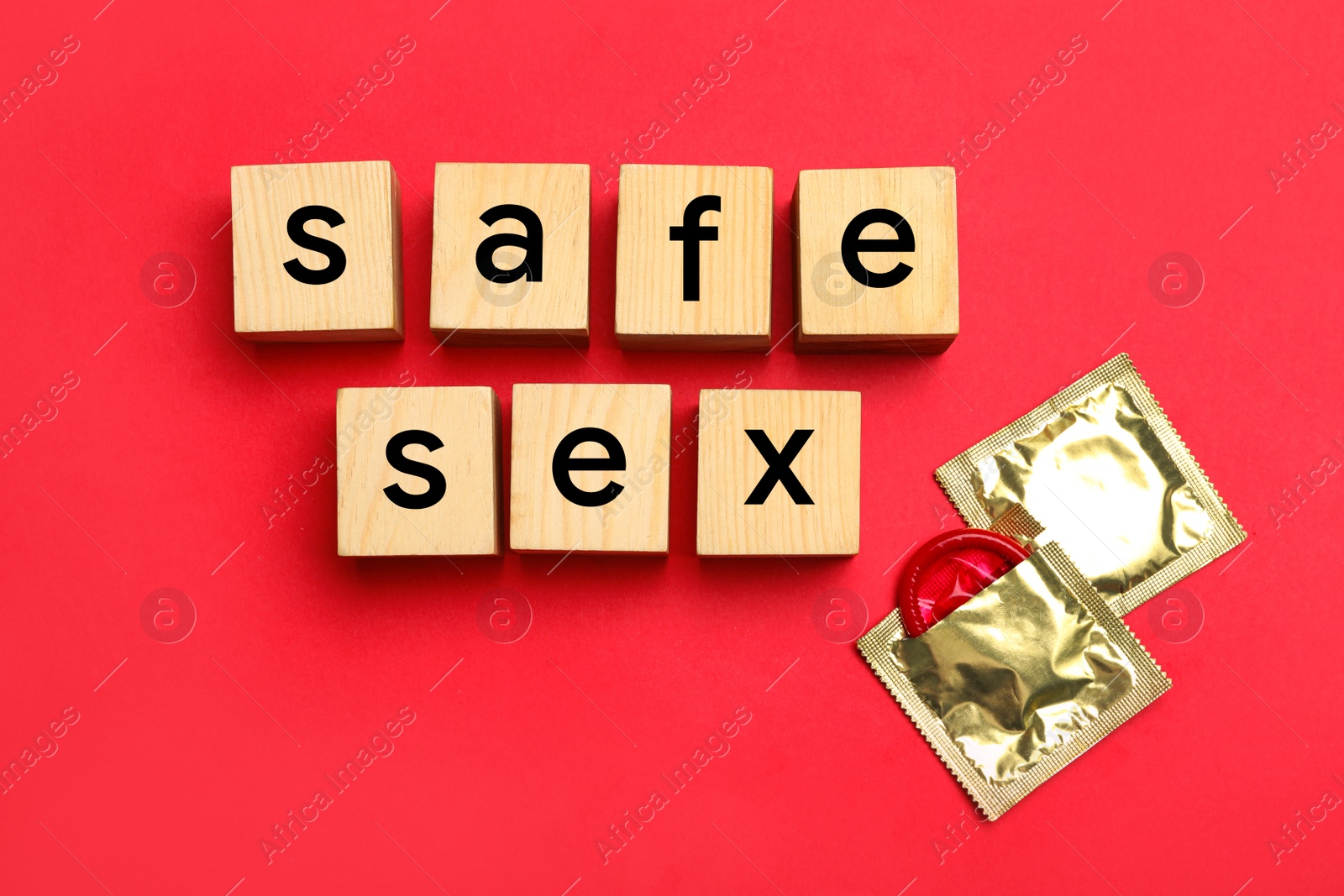 Photo of Words SAFE SEX made with wooden cubes and shiny condoms on red background, flat lay