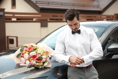 Photo of Young handsome man with beautiful flower bouquet near car outdoors