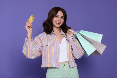 Photo of Beautiful young woman with paper shopping bags and credit card on purple background