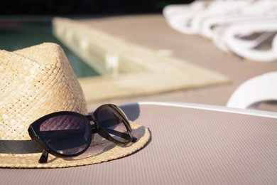 Photo of Stylish hat and sunglasses on sunbed near outdoor swimming pool, space for text