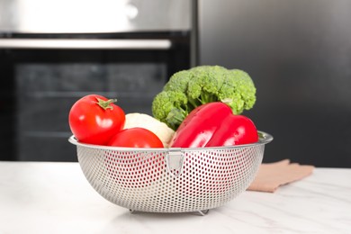 Photo of Colander with different fresh vegetables on white marble table in kitchen