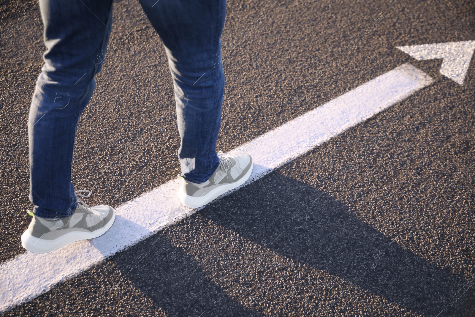 Image of Planning future. Man walking on drawn mark on road, closeup. White arrow showing direction of way