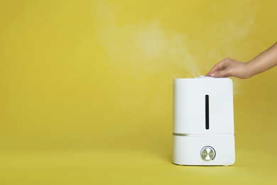 Photo of Woman using modern air humidifier on yellow background, closeup. Space for text