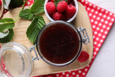 Photo of Jar of delicious raspberry jam, fresh berries and green leaves on white table, top view