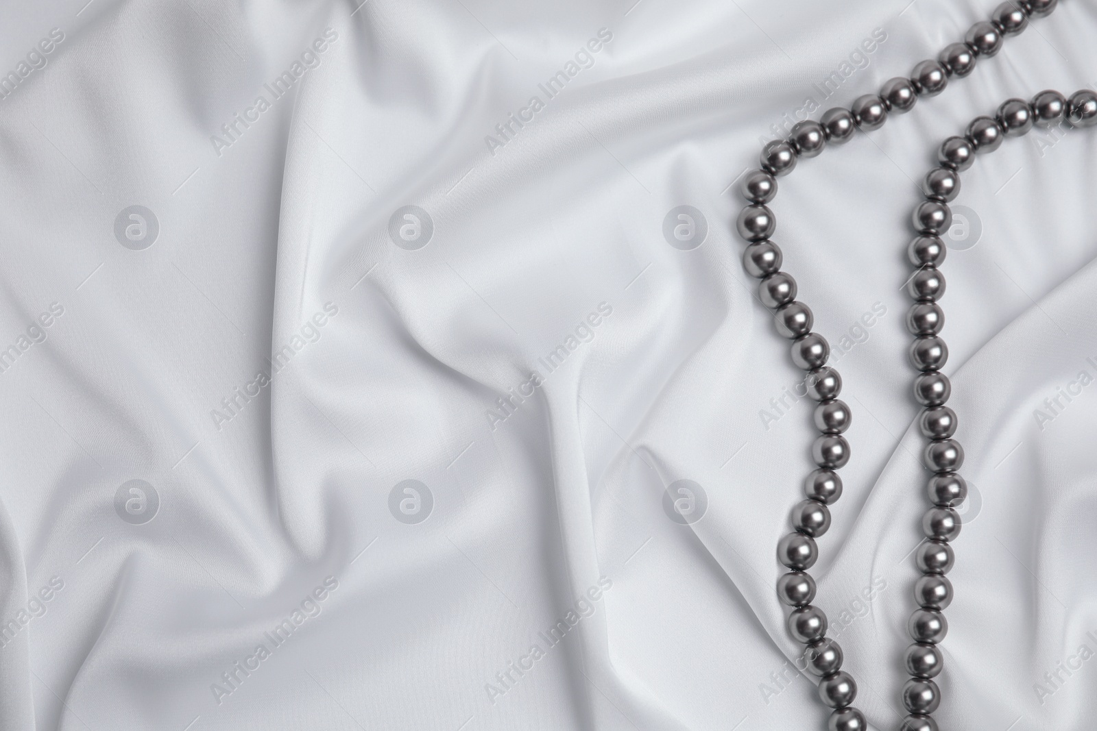 Photo of Beautiful pearls on white silk, top view. Space for text