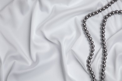Photo of Beautiful pearls on white silk, top view. Space for text