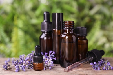 Photo of Bottles with natural lavender essential oil on wooden table against blurred background