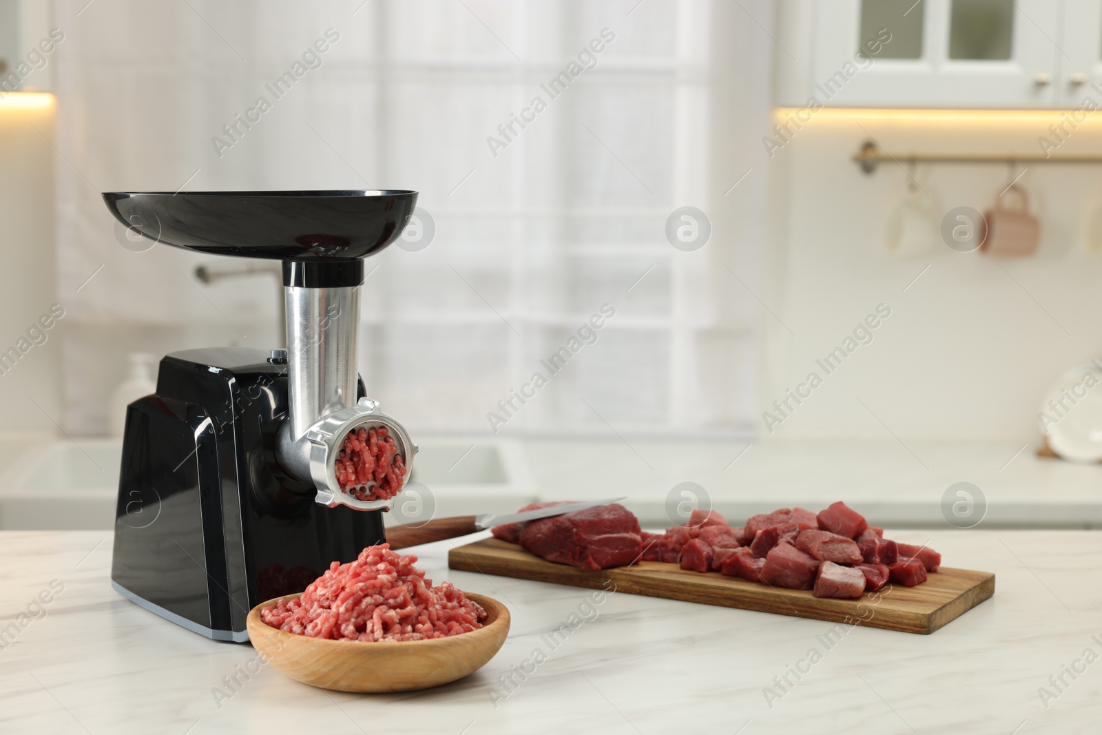 Photo of Electric meat grinder with minced beef on white marble table in kitchen, space for text