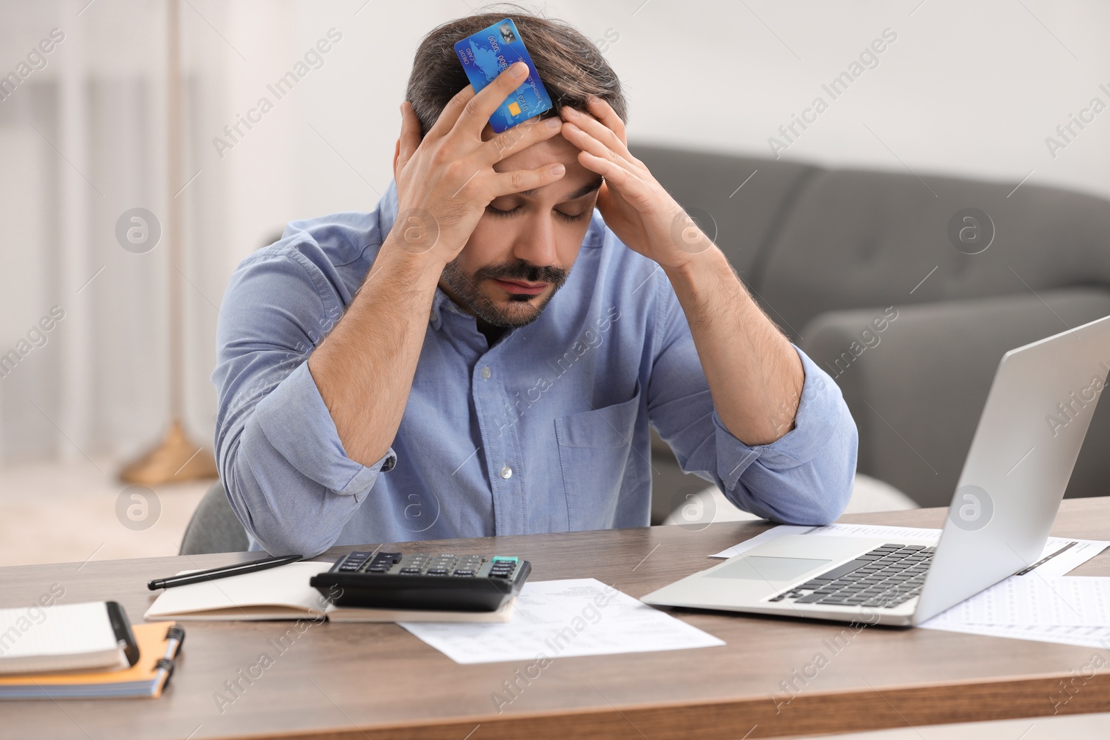 Photo of Confused man with debt notification and credit card planning budget at table in room. Financial problem