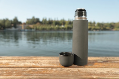 Photo of Modern grey thermos on wooden surface near river. Space for text