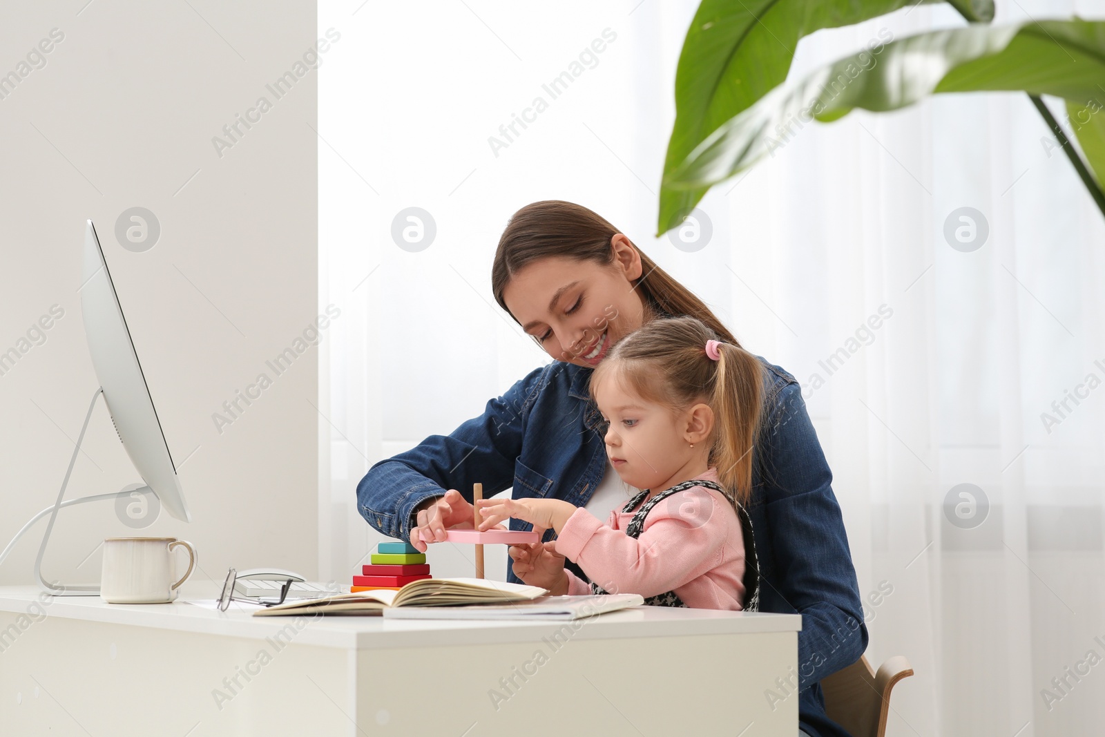 Photo of Mother playing with her daughter at desk. Taking break in remote work at home