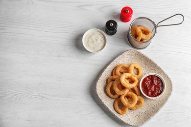 Plate with tasty onion rings and sauces on table, top view