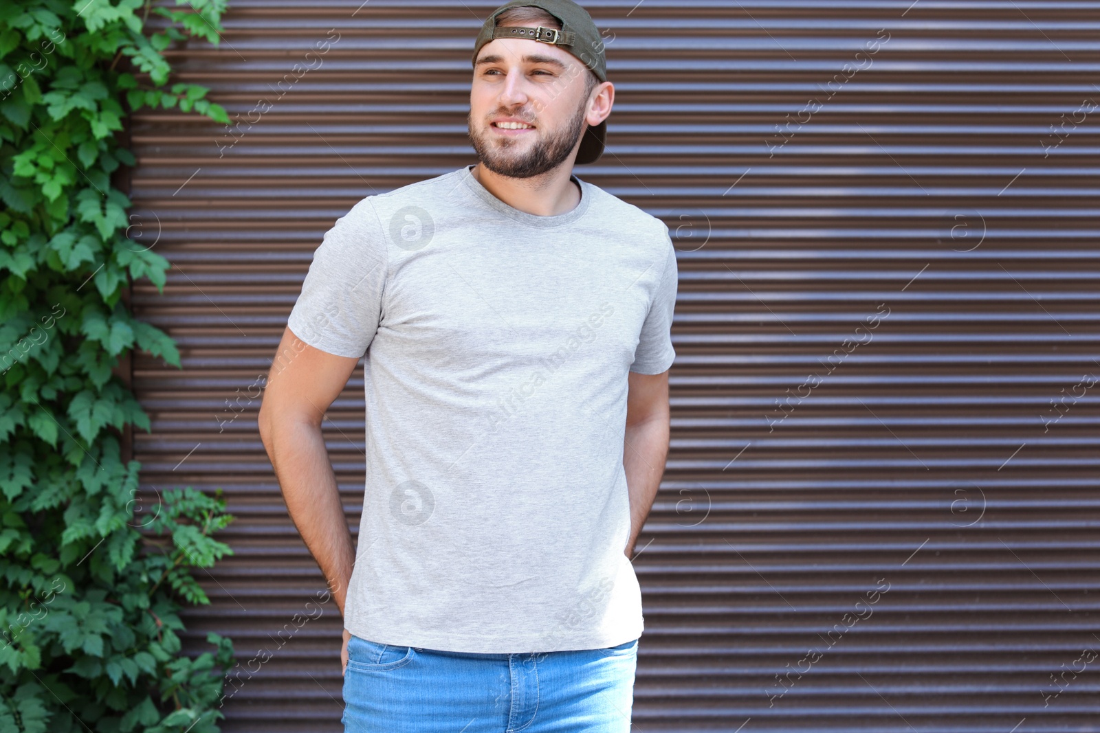 Photo of Young man wearing gray t-shirt near wall on street. Urban style