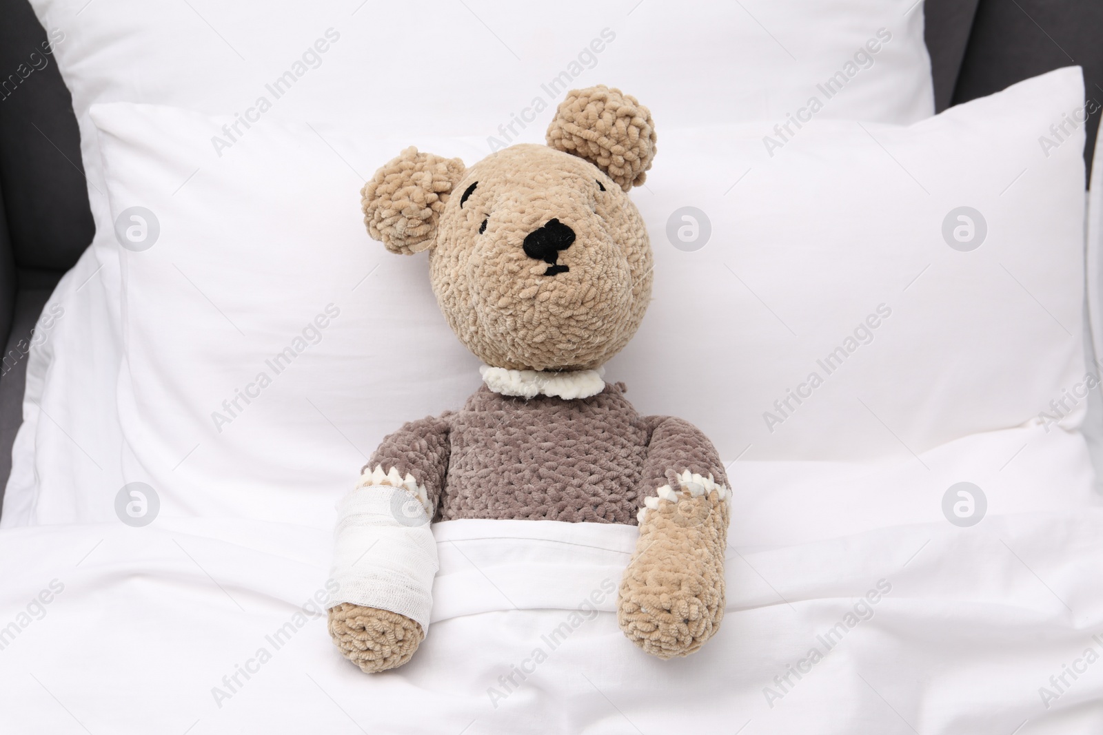 Photo of Toy cute bear with bandage under blanket in bed