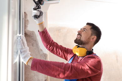 Photo of Worker using foam gun for window installation indoors