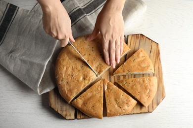 Photo of Woman cutting bread on wooden background, top view