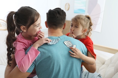 Photo of Cute little children sticking paper fish to father's back at home