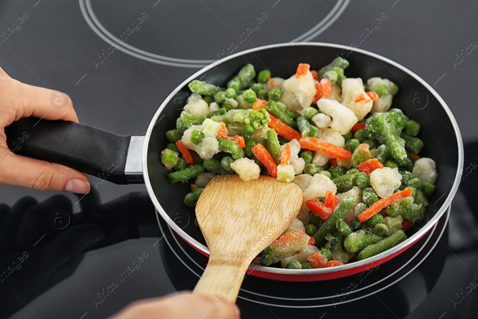 Photo of Woman cooking frozen vegetable mix on induction stove, closeup