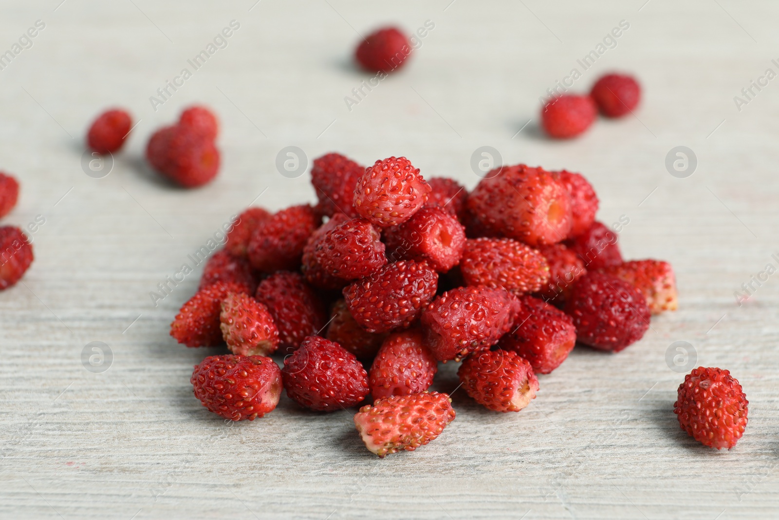 Photo of Pile of wild strawberries on white wooden table, closeup